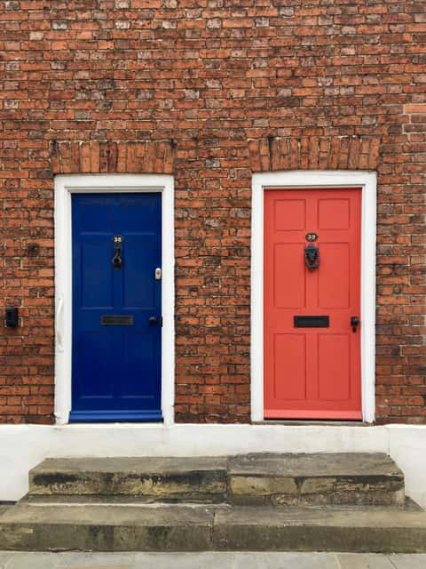 Two front doors side by side in a brick terrace, one navy blue and one coral, each with its own house number.