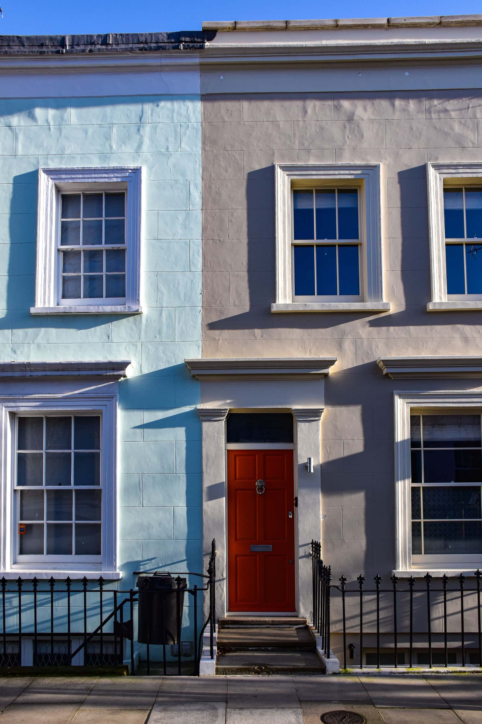 Two terraced houses sharing a party wall, one painted pale blue and one grey, each with its own front door.